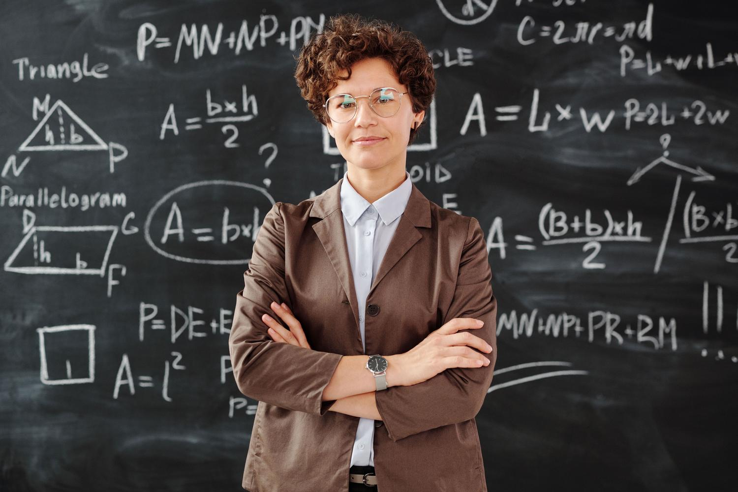 Docente de secundaria frente a una pizarra Docente de secundaria frente a una pizarra con esquemas matemáticos, simbolizando el dominio del temario y la fase de examen.