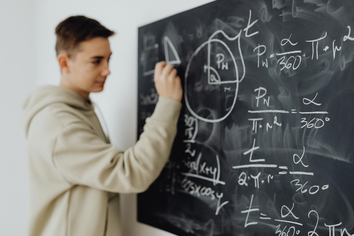 Estudiante adolescente concentrado resolviendo una ecuación en una pizarra, simbolizando el desarrollo del razonamiento lógico y el pensamiento matemático avanzado. Estudiante adolescente concentrado resolviendo una ecuación en una pizarra, simbolizando el desarrollo del razonamiento lógico y el pensamiento matemático avanzado.
