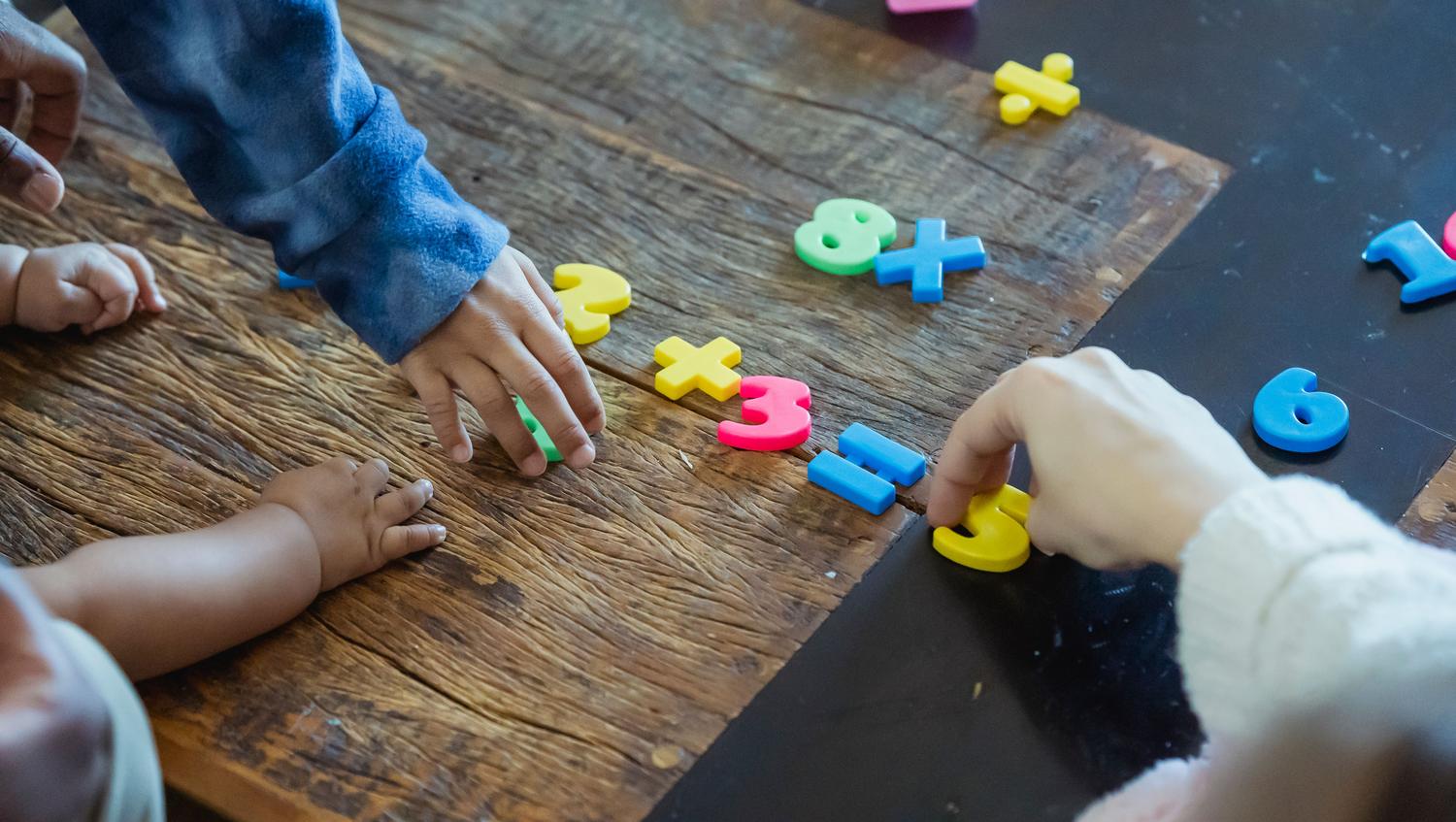 Niños manipulando números de plástico coloridos sobre una mesa de madera, representando la etapa inicial del aprendizaje matemático a través de objetos físicos. Niños manipulando números de plástico coloridos sobre una mesa de madera, representando la etapa inicial del aprendizaje matemático a través de objetos físicos.