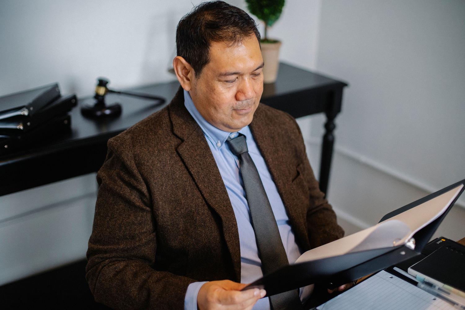 Abogado analizando un informe legal en una carpeta con un mazo judicial visible en el escritorio Abogado analizando un informe legal en una carpeta con un mazo judicial visible en el escritorio