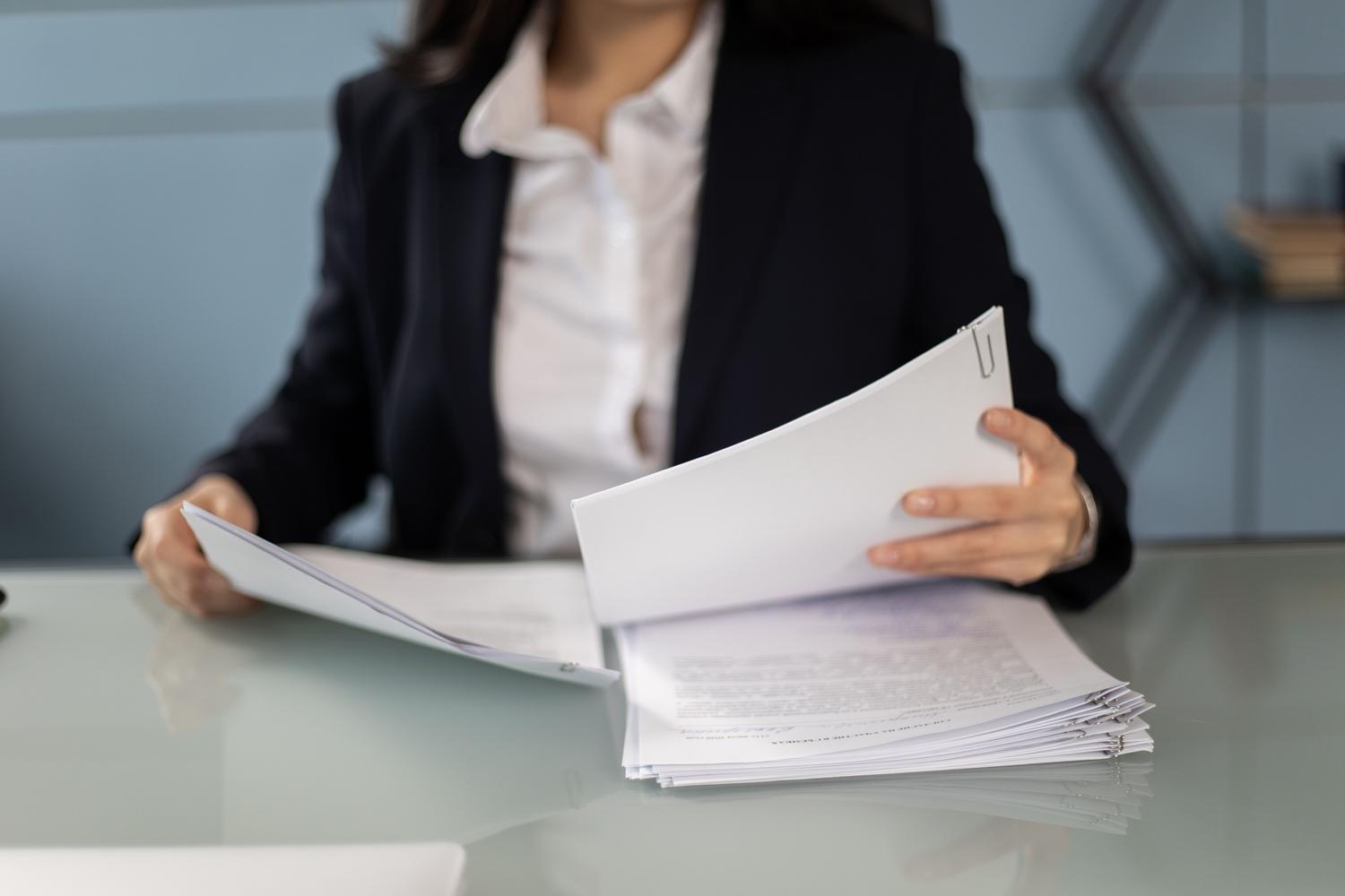 Primer plano de manos de profesional legal revisando un expediente documental grueso en un escritorio de oficina Primer plano de manos de profesional legal revisando un expediente documental grueso en un escritorio de oficina