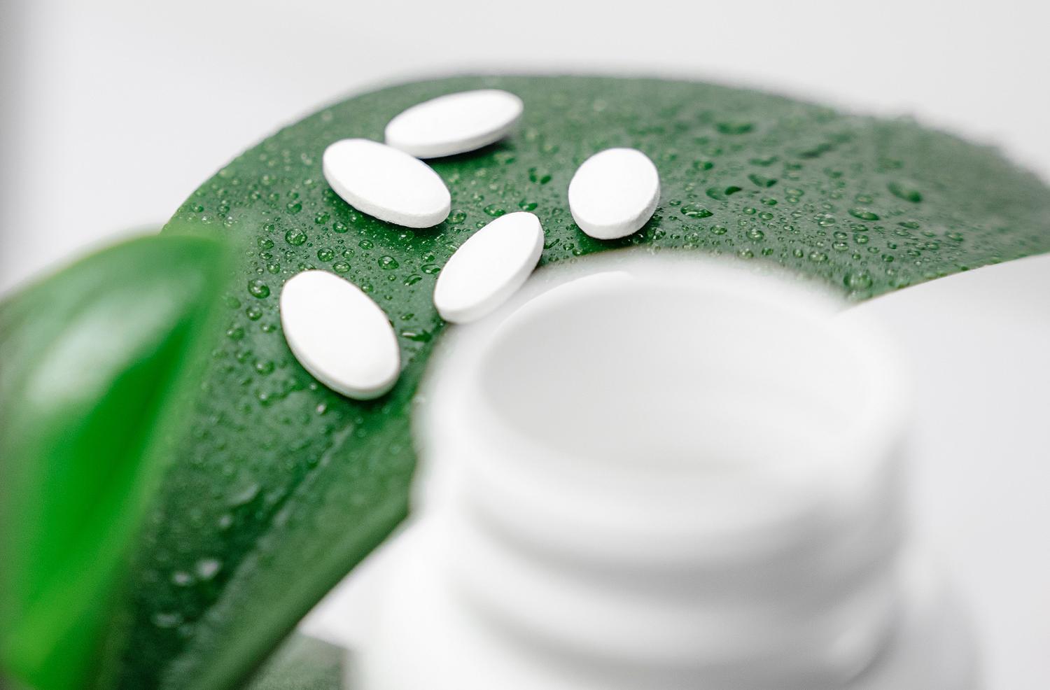 Pastillas blancas sobre una hoja verde con gotas de rocío, simbolizando la sostenibilidad farmacéutica y el Pacto Verde Europeo. Pastillas blancas sobre una hoja verde con gotas de rocío, simbolizando la sostenibilidad farmacéutica y el Pacto Verde Europeo.