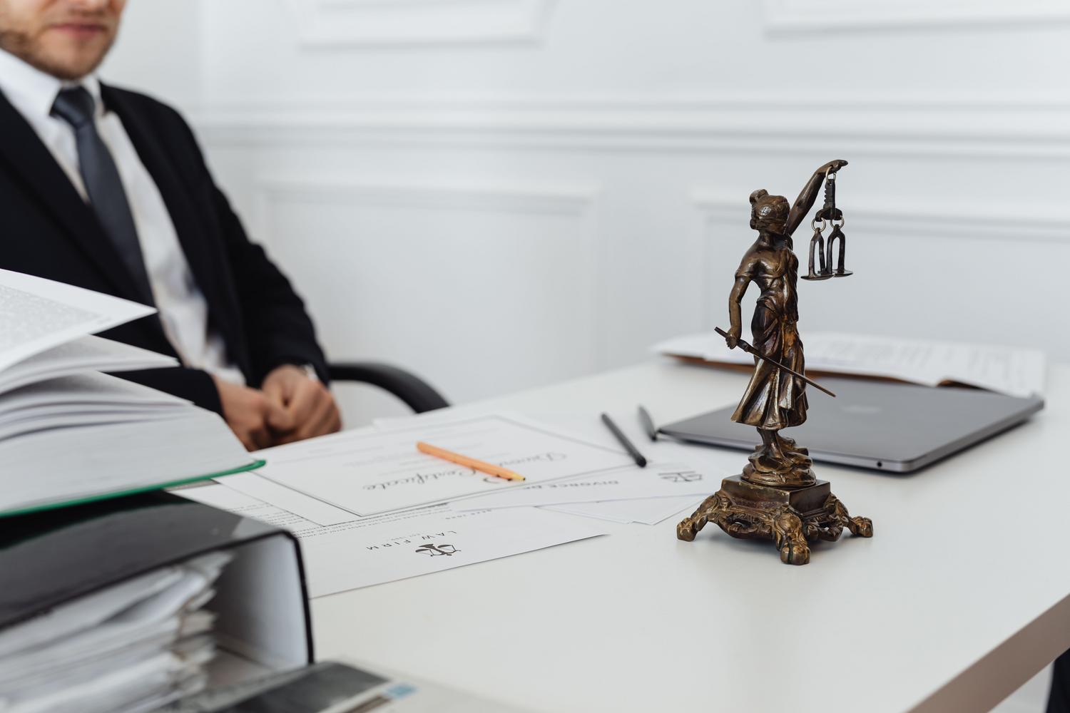 Espacio de trabajo jurídico con una estatua de la justicia, ordenador portátil y expedientes, reflejando la gestión diaria de la carrera judicial. Espacio de trabajo jurídico con una estatua de la justicia, ordenador portátil y expedientes, reflejando la gestión diaria de la carrera judicial.