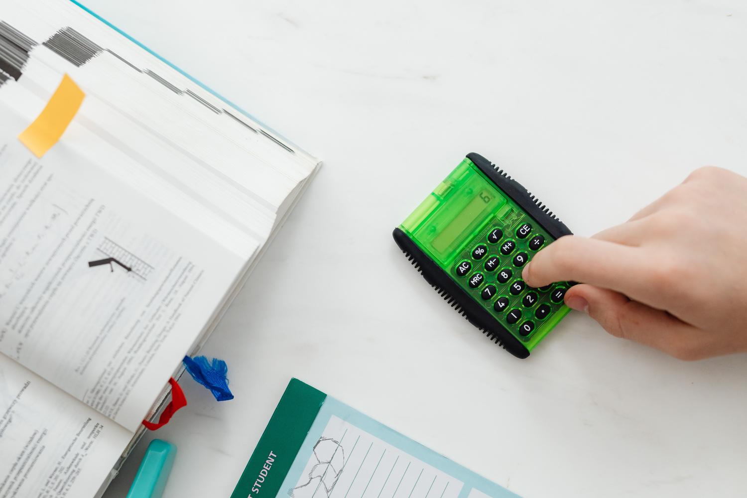Primer plano de un estudiante utilizando una calculadora junto a un libro de texto de matemáticas. Primer plano de un estudiante utilizando una calculadora junto a un libro de texto de matemáticas.