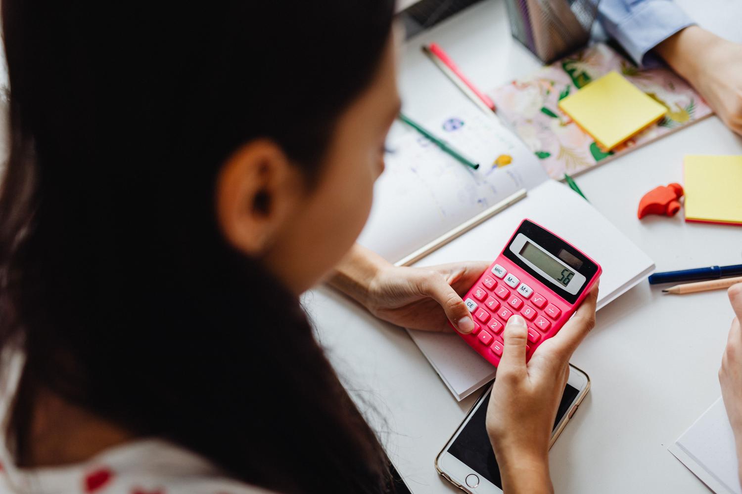 Niña de primaria concentrada resolviendo problemas matemáticos con una calculadora rosa. Niña de primaria concentrada resolviendo problemas matemáticos con una calculadora rosa.